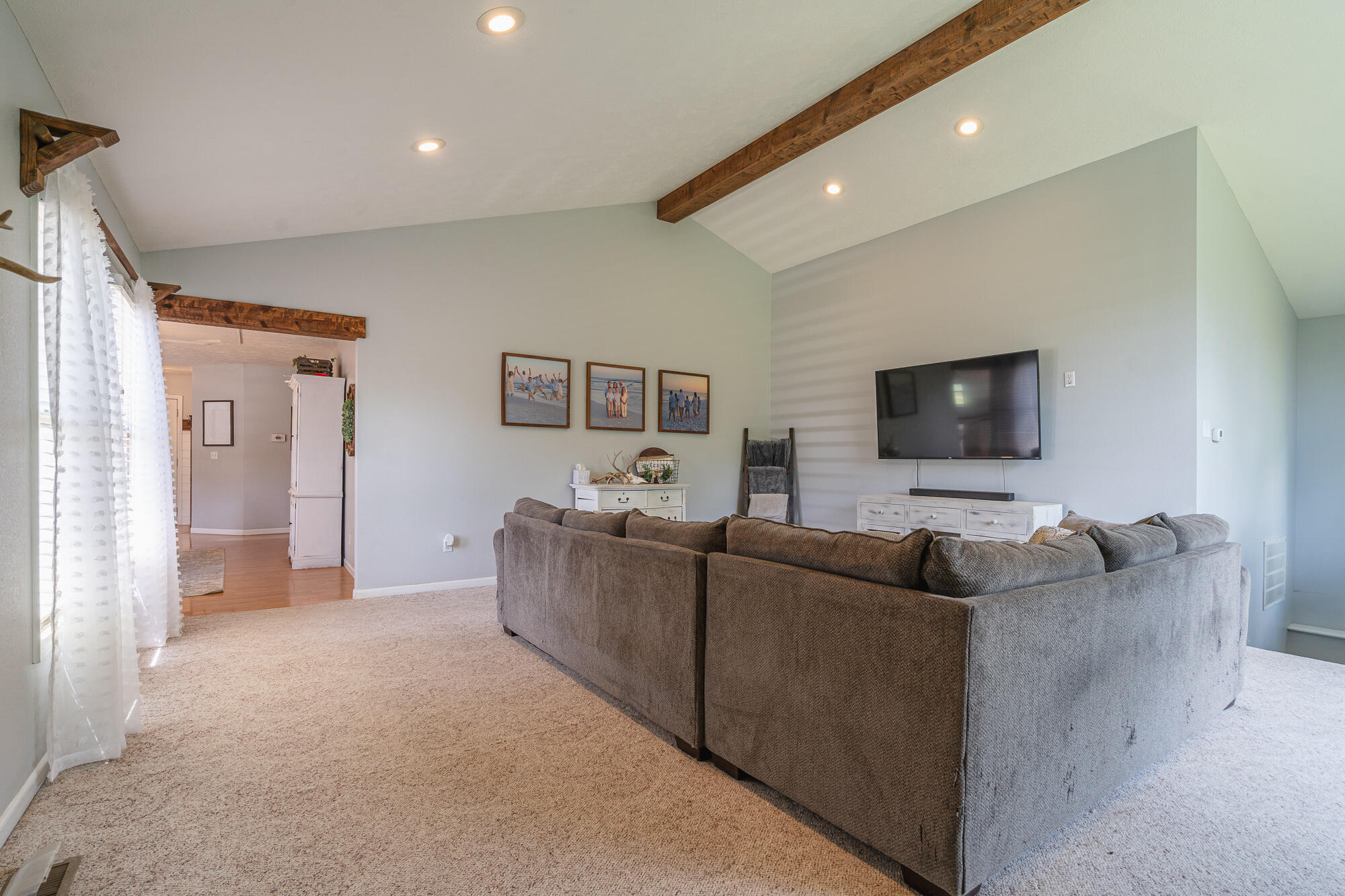 Living room with a large gray sectional sofa, vaulted ceiling, and exposed wooden beams.