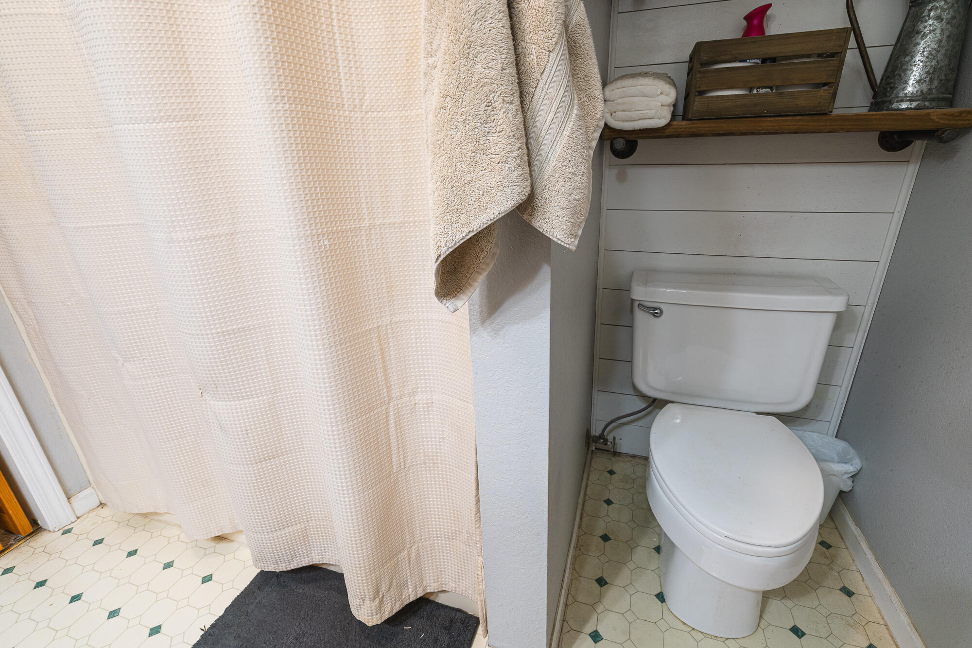 Bathroom with a white toilet, cream shower curtain, and hexagonal tile floor with green accents.