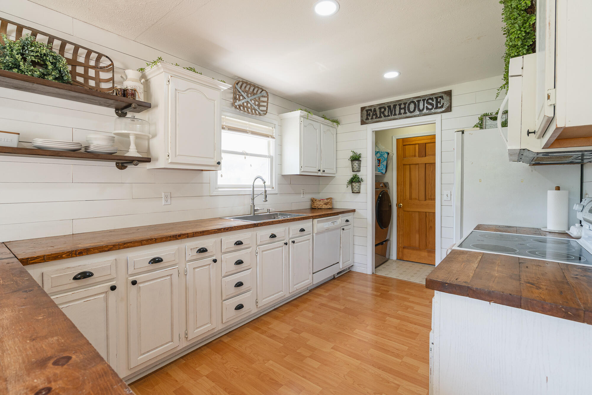 Farmhouse kitchen with white cabinets, dark wood countertops, open shelves, and a sink beneath the window.