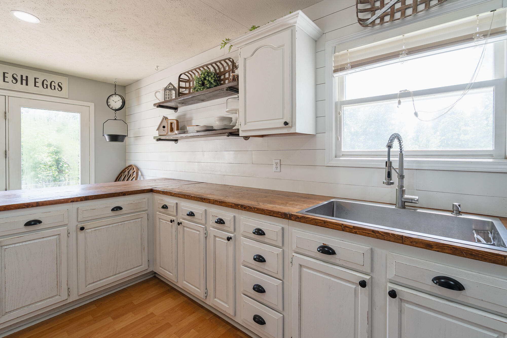 Farmhouse kitchen with white cabinets, dark wood countertops, and a large sink beneath a window.
