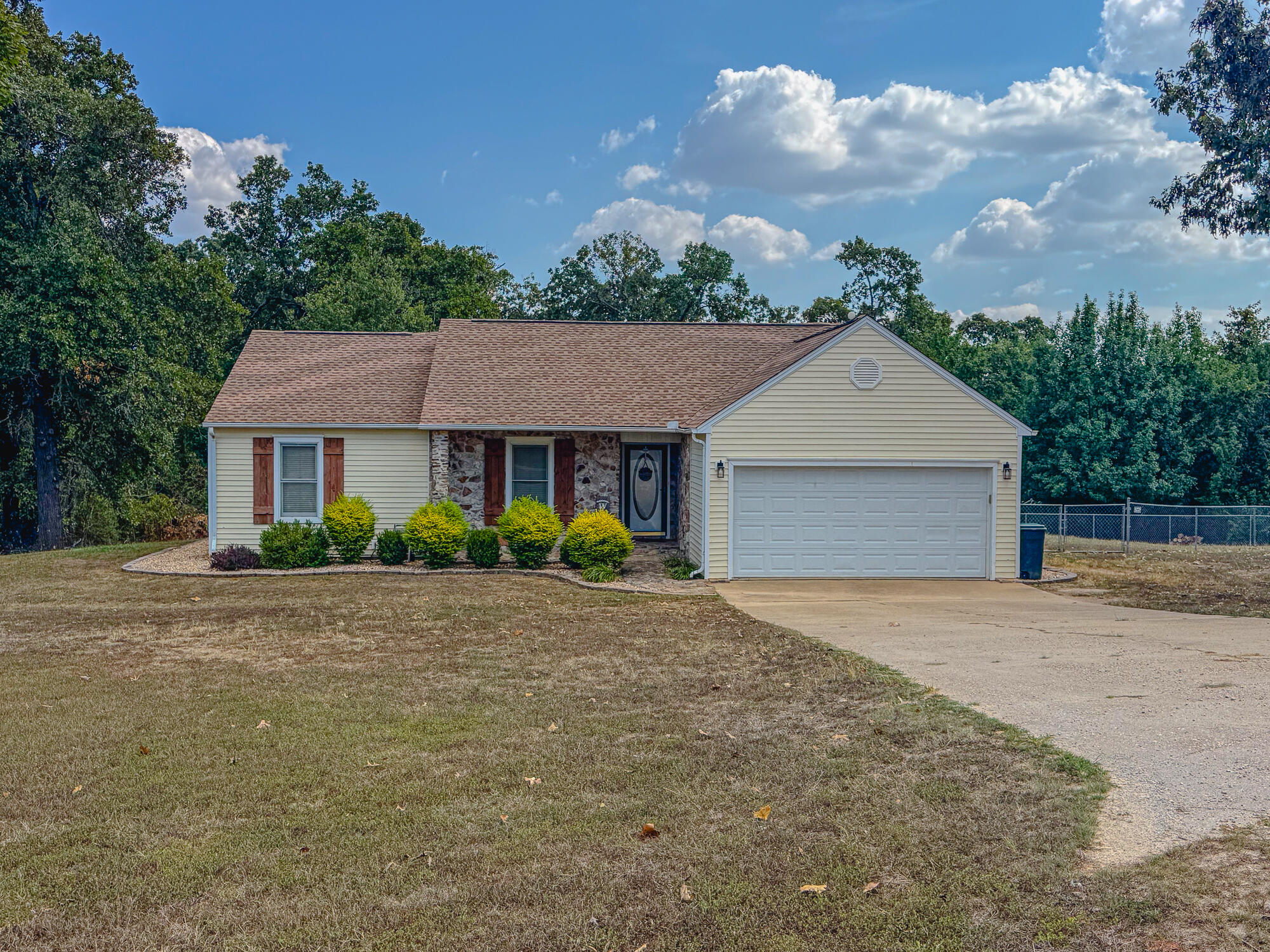 Single-story beige house with stone façade accents, a two-car garage, and a curved driveway.