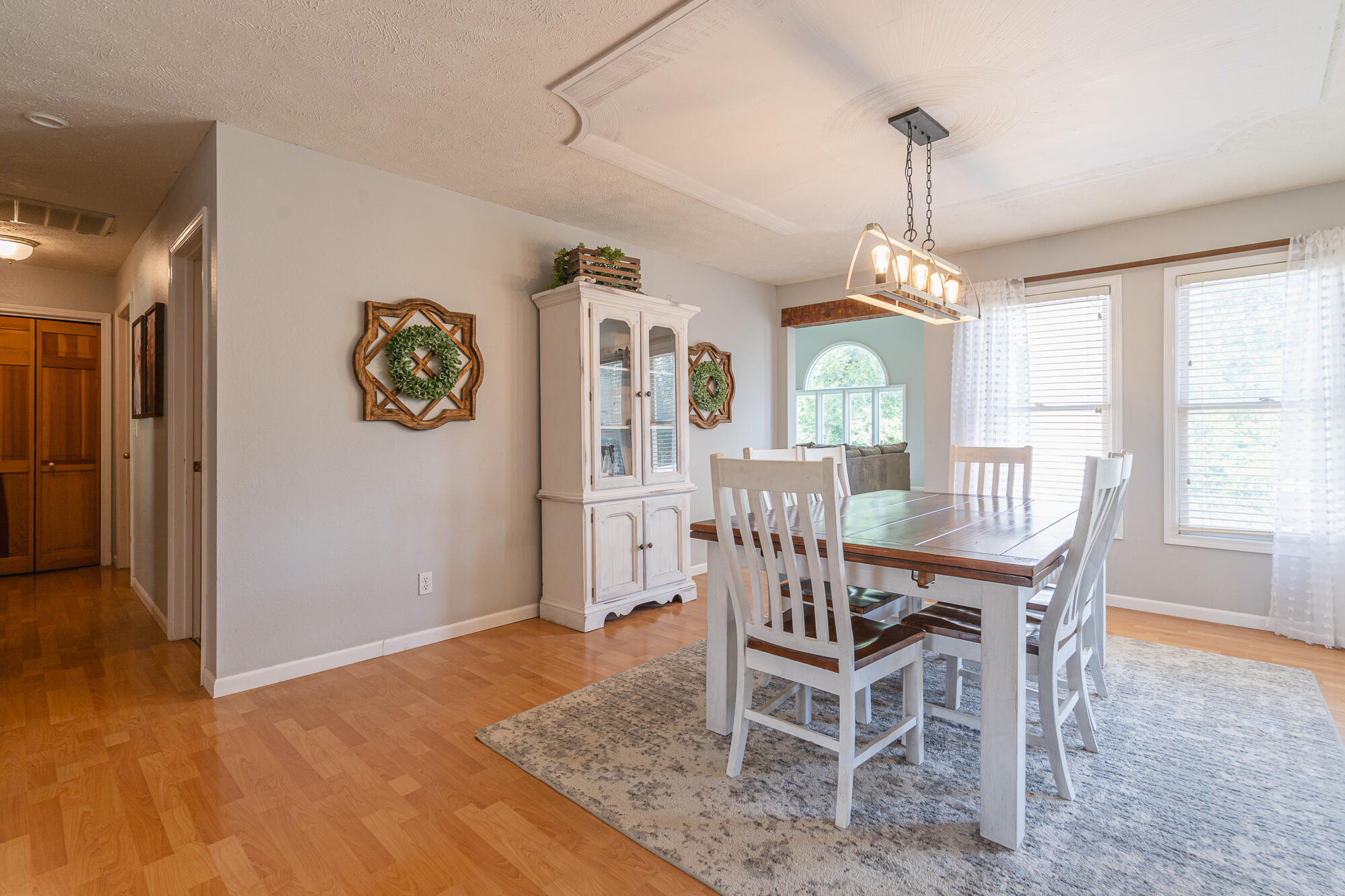 Dining room with a wooden table, white chairs, china cabinet, and arched window.