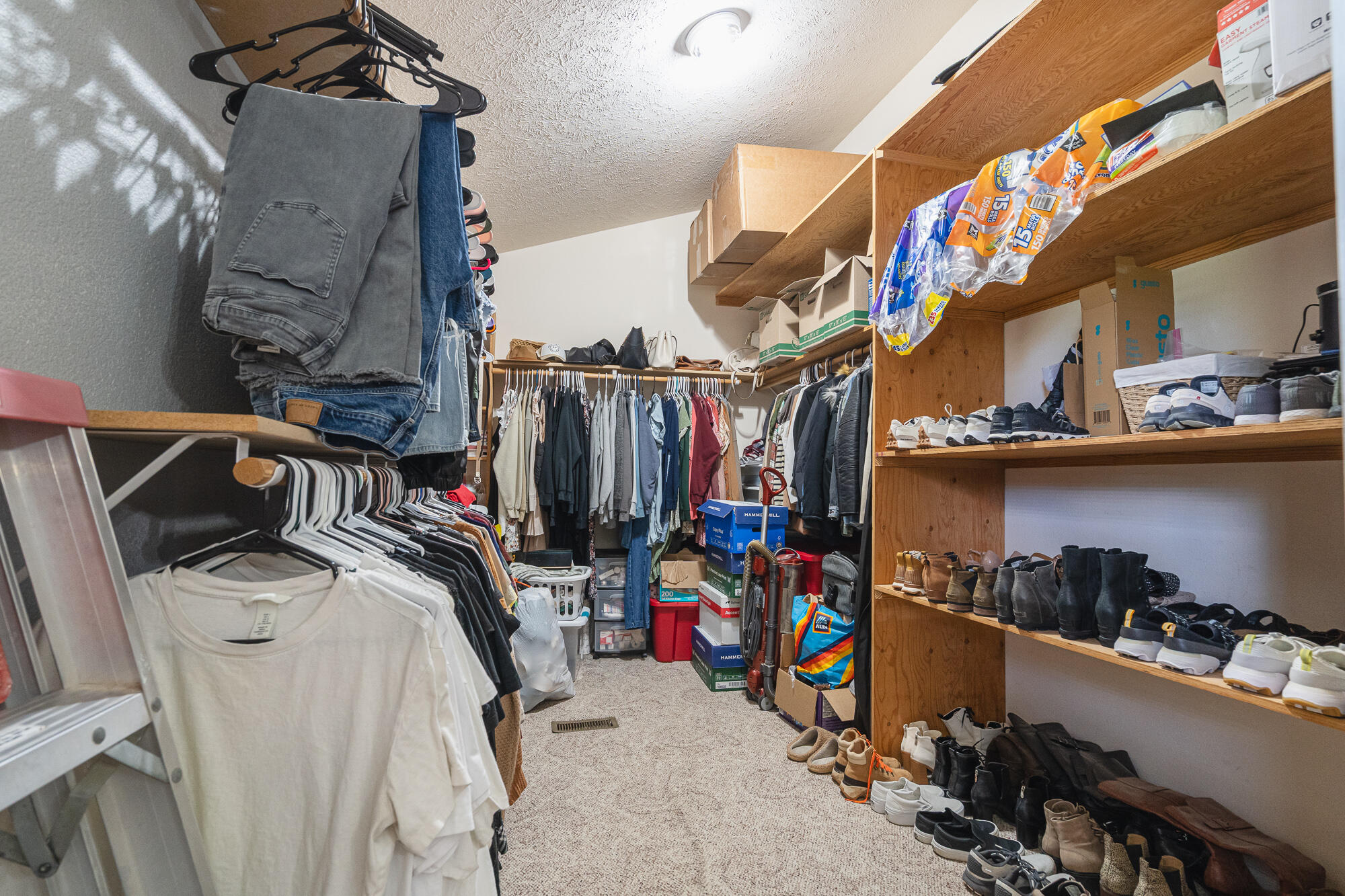 Walk-in closet with hanging clothes, extensive shoe shelving, and storage boxes.