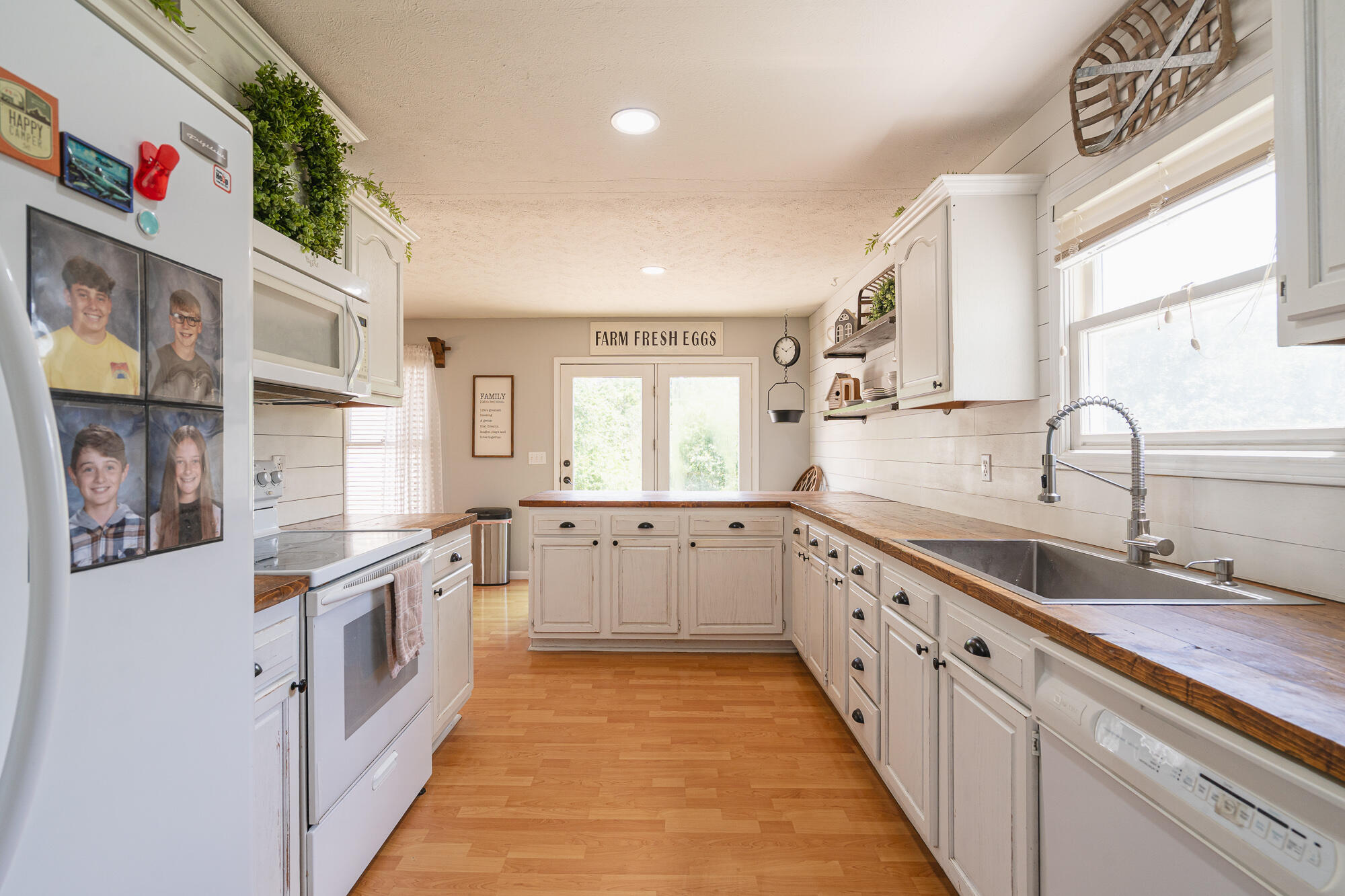Farmhouse kitchen with white cabinets, wood countertops, a central peninsula, and a large window over the sink.
