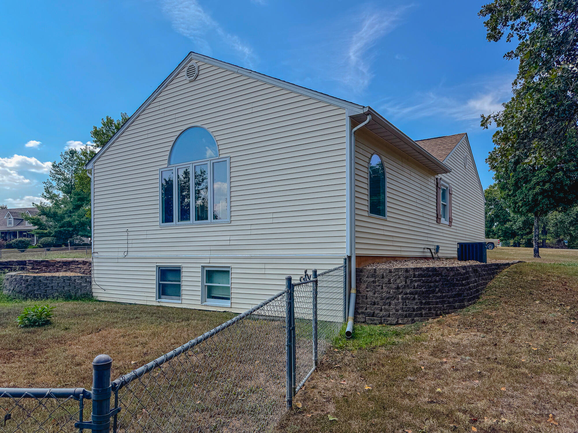 House side with arched windows, chain-link fencing, and stone retaining walls.
