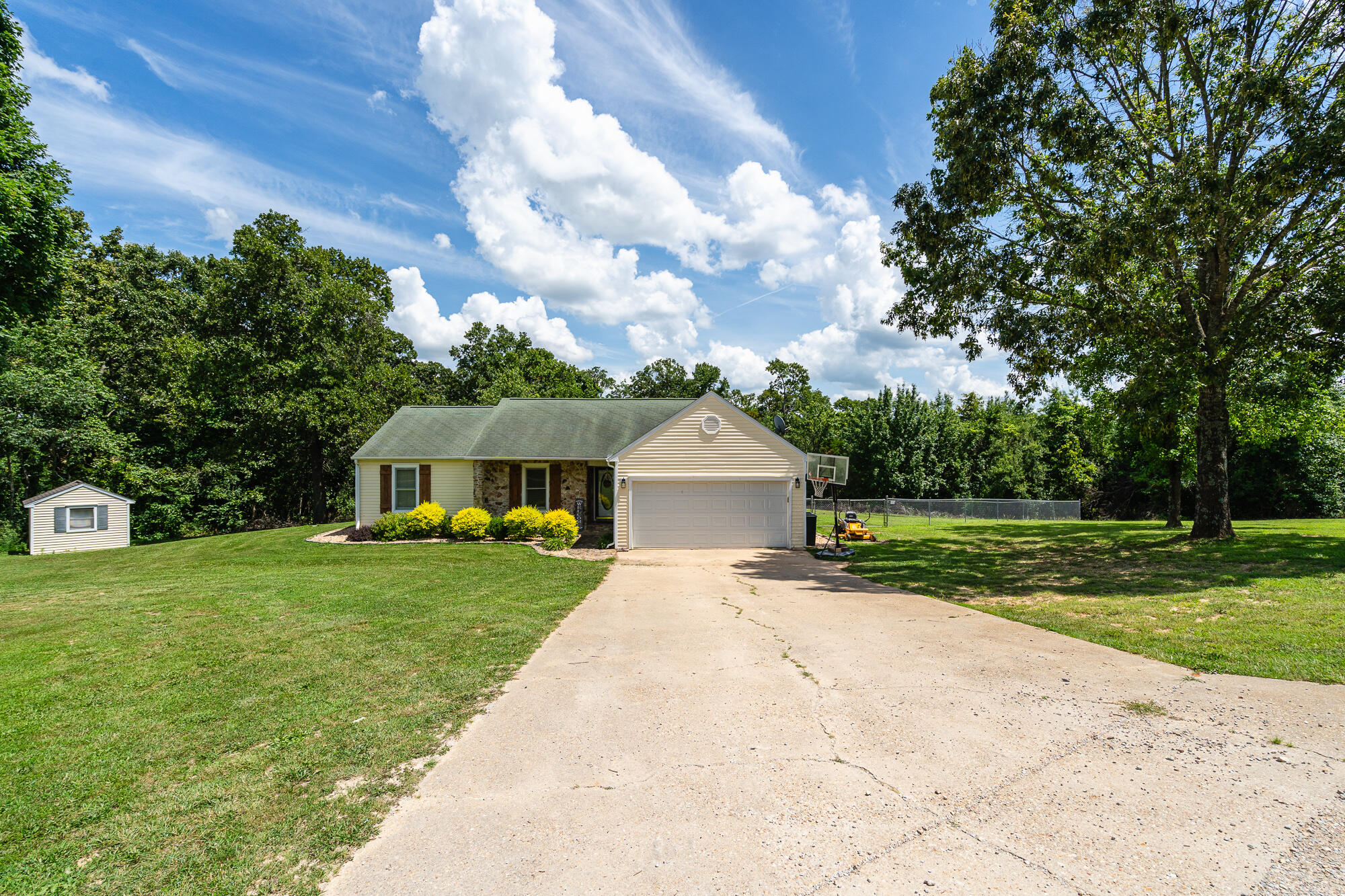 Single-story home with an attached garage, wide driveway, and a small shed in the grassy yard.