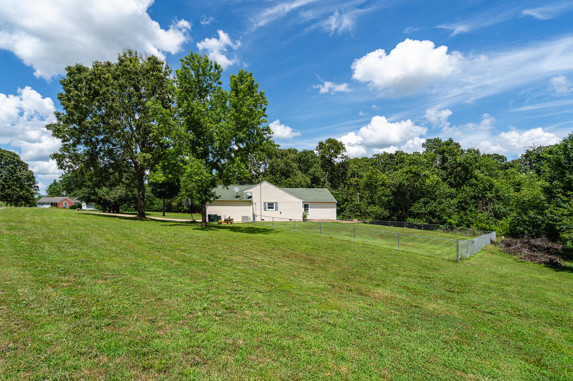 Single-story home beyond a broad lawn, with a fenced yard and mature trees.
