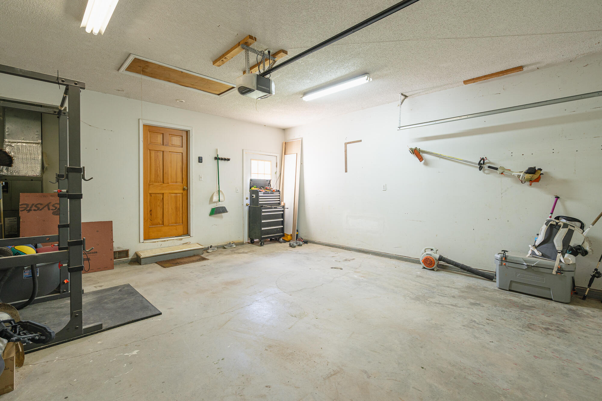 Garage workshop with a concrete floor, wooden entry door, tool chest, and equipment along the walls.