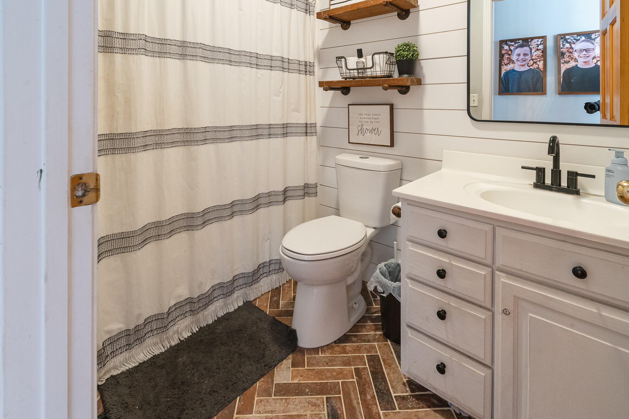 Bathroom with a white vanity, black faucet, striped shower curtain, and brick-pattern tile floor.