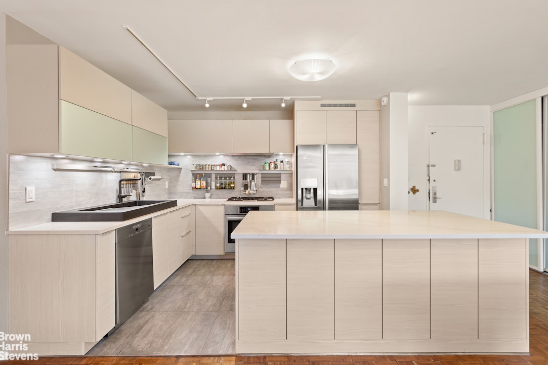 Modern kitchen with pale wood cabinets, stainless steel appliances, and a large central island.