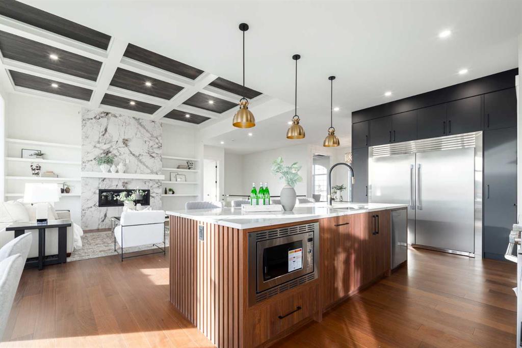 Open-plan kitchen with a wood-paneled island, dark cabinets, and a marble fireplace in the adjoining living area.
