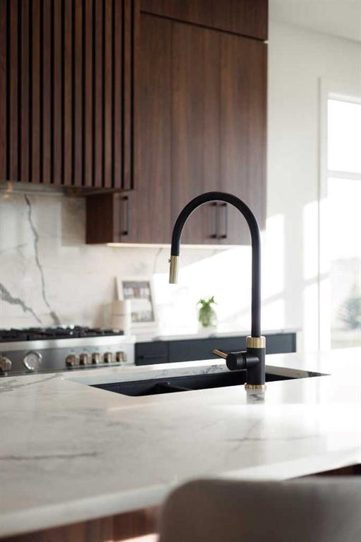 Modern kitchen with a marble island, black-and-brass faucet, dark wood cabinets, and stainless steel range.