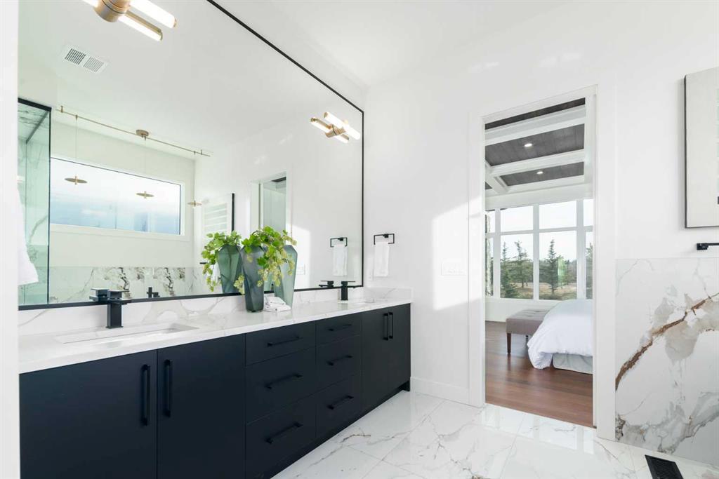 Modern bathroom with a dark double vanity, marble surfaces, and an open doorway to a bright bedroom.