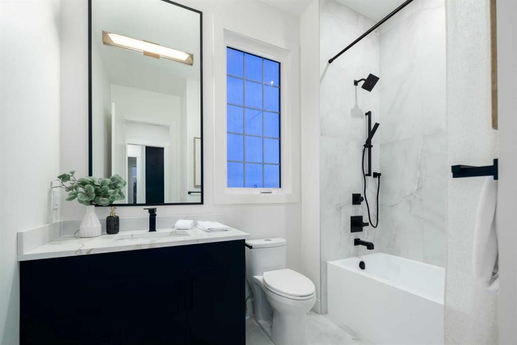 Modern bathroom with a navy vanity, black-framed mirror, tall window, and marble-look tub-shower.