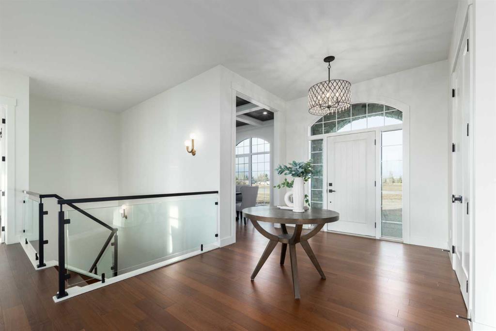 Bright entry foyer with arched windows, a glass-railed staircase, and dark hardwood floors.