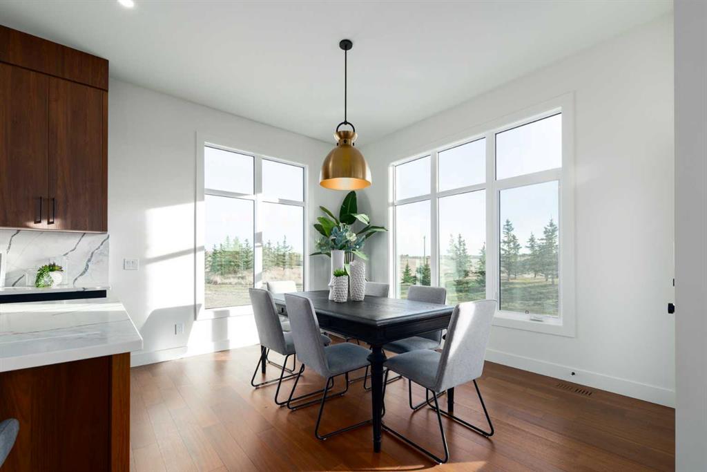 Dining area with a dark table and gray chairs beside large windows overlooking trees.