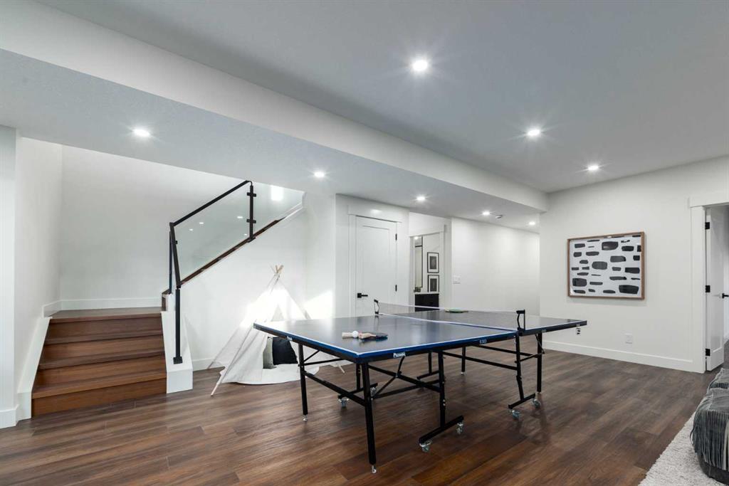 Basement recreation room with a ping-pong table, glass-railed stairs, and a small play tent.