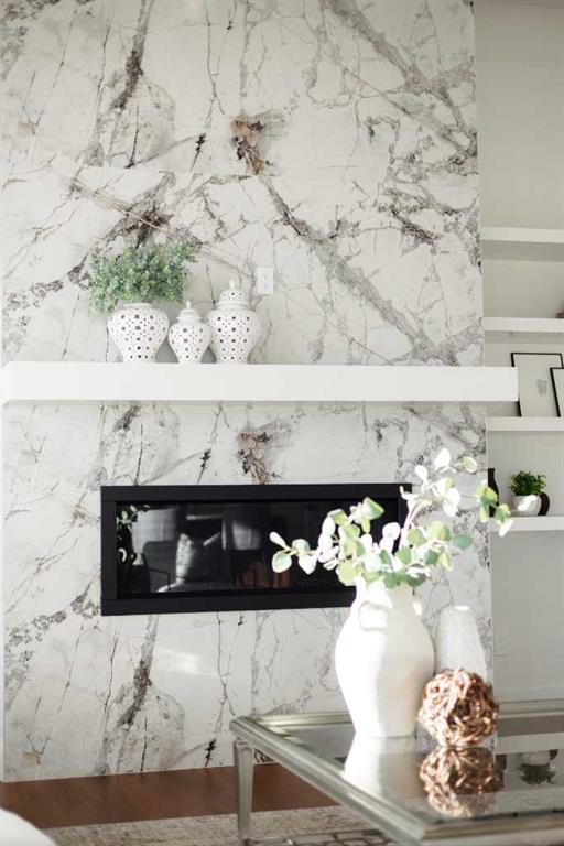 Living room fireplace set in a veined marble wall, with a white mantel and glass coffee table.