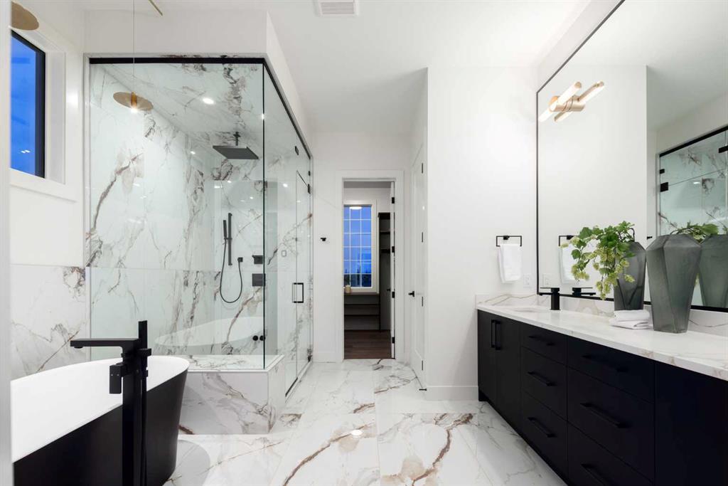 Marble bathroom with glass-enclosed shower, freestanding tub, and dark double vanity.
