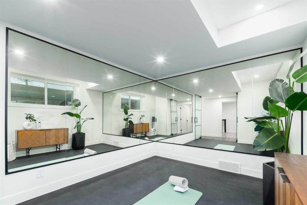 Home exercise room with mirrored walls, a yoga mat, and potted plants.