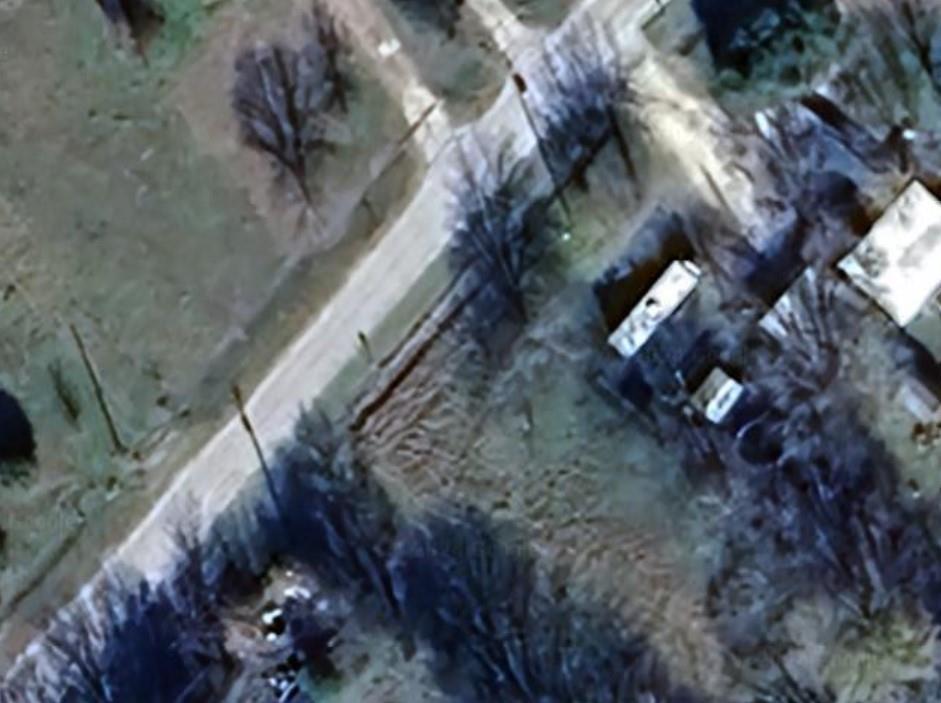 Aerial view of a partly wooded vacant lot beside a road, with nearby buildings.