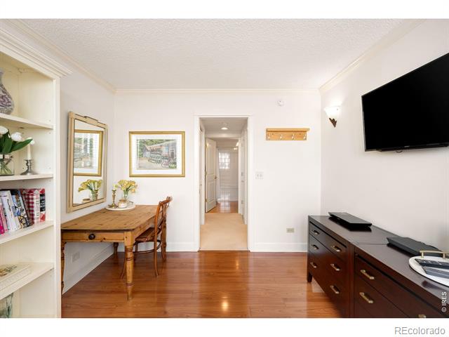 Furnished condo room with a wooden table, built-in shelves, wall-mounted television, and hardwood floors.