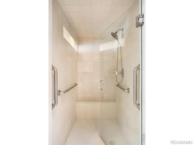 Walk-in shower with beige tile, glass door, grab bars, and handheld showerhead.