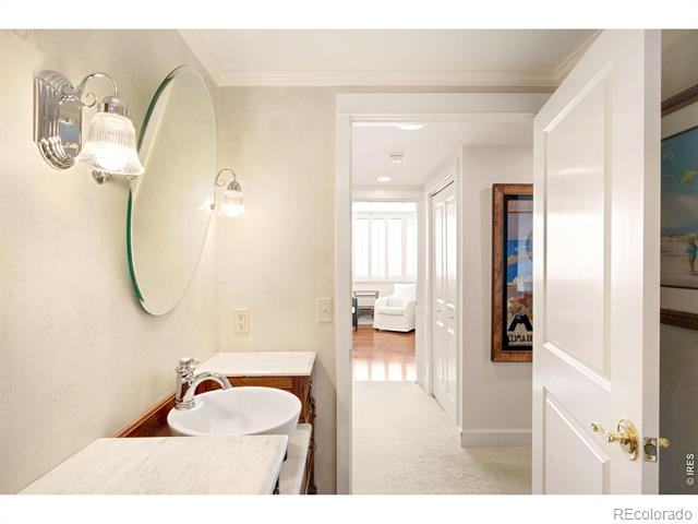 Bathroom vanity with a vessel sink and oval mirror, looking down a hallway toward a bright living area.