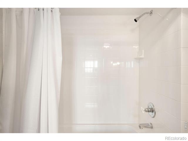 White-tiled bathtub and shower with chrome fixtures and a white curtain.