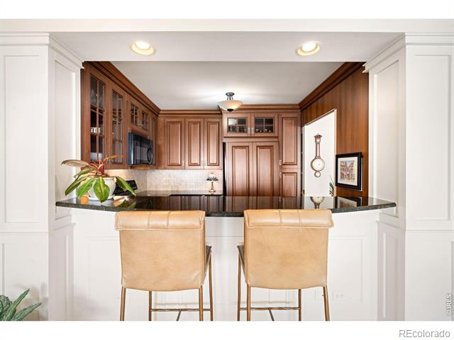 Kitchen with dark wood cabinetry, a granite breakfast bar, and two tan leather stools.