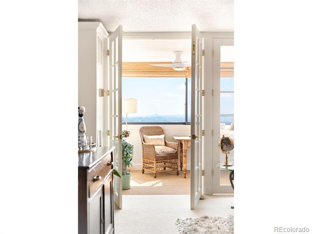 Bright sitting area with a wicker armchair beside a large window overlooking the distant city.