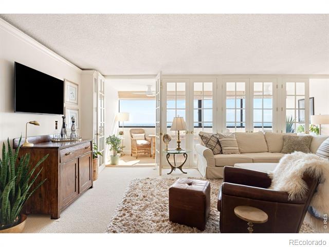 Furnished living room with a beige sofa, leather chairs, and French doors to a sunny sitting area.