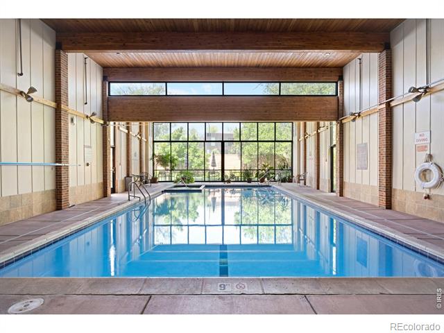 Indoor swimming pool with blue water, large windows, and an exposed wood-beam ceiling.