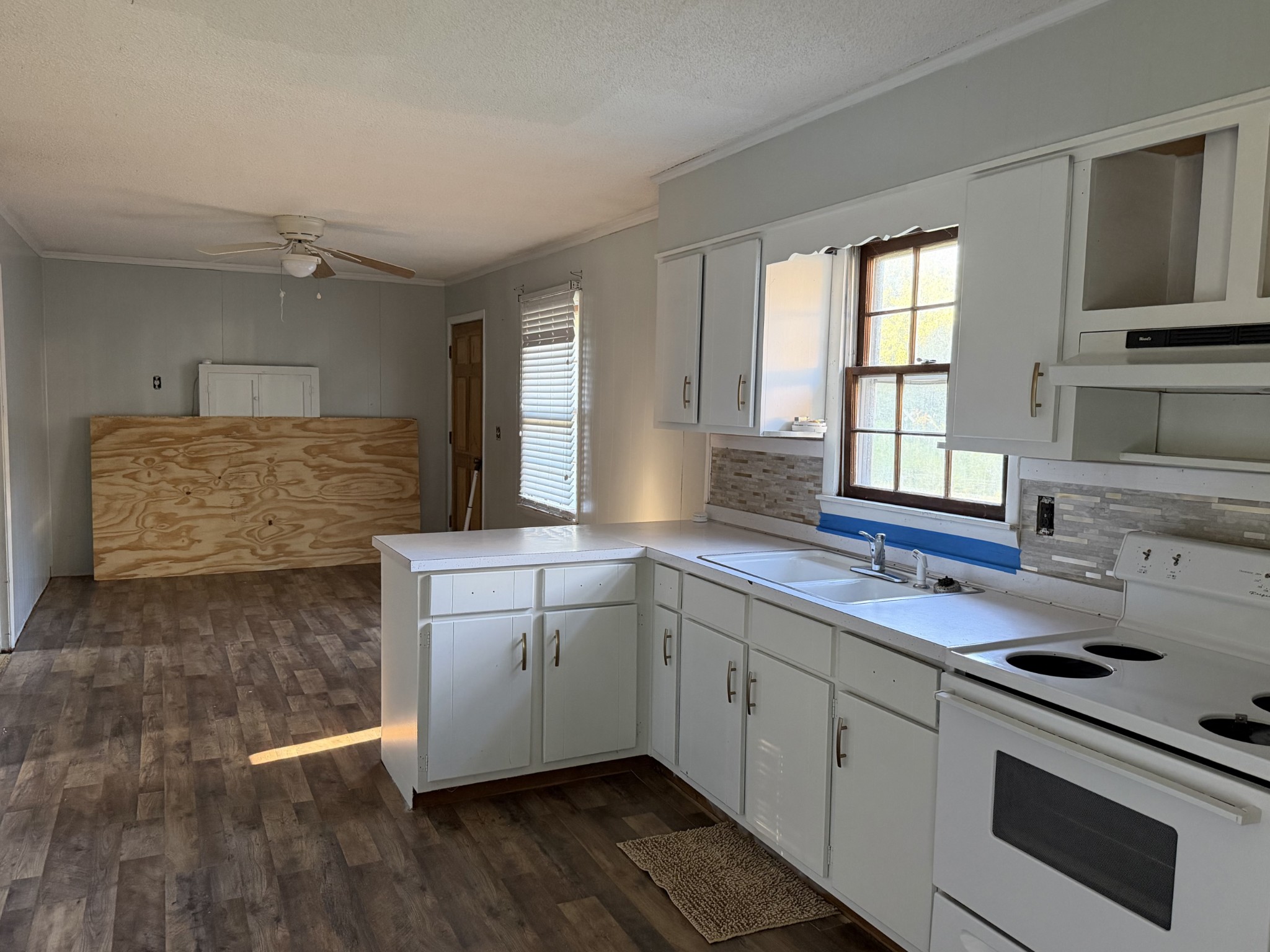 Kitchen with white cabinets, an electric range, and plywood leaning in the adjoining open area.