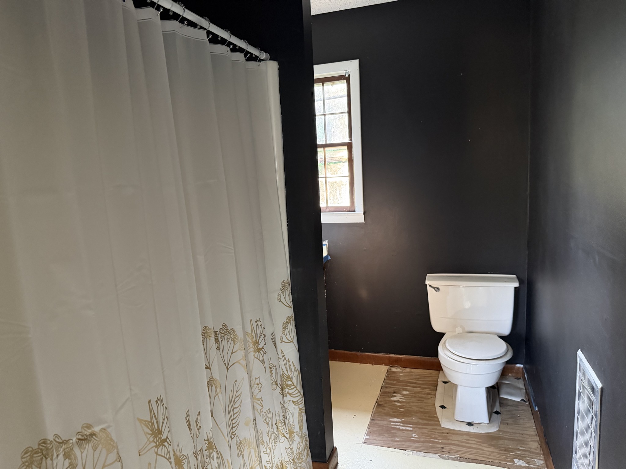 Bathroom with dark walls, a white toilet, patterned shower curtain, and narrow window.