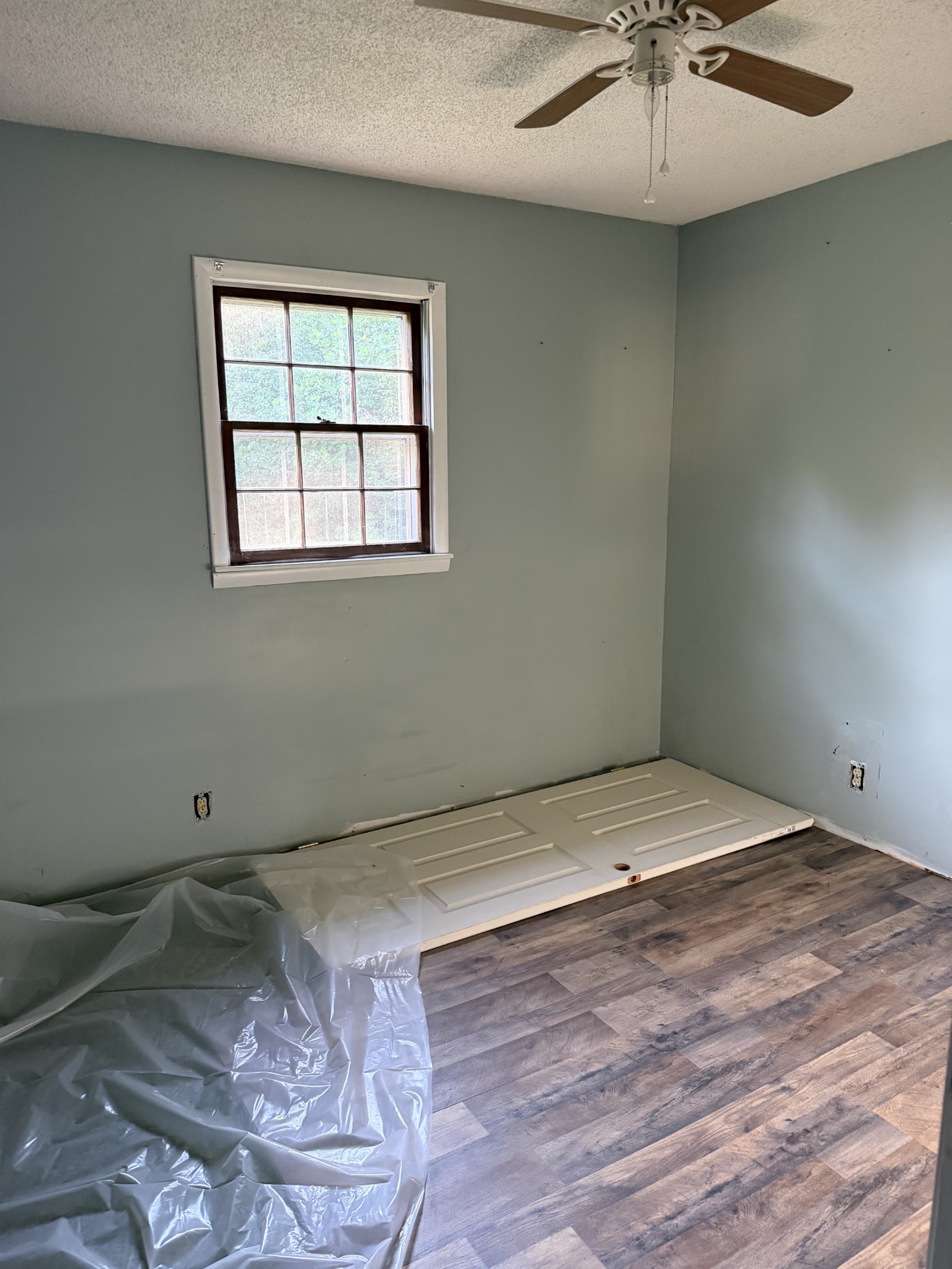 Unfinished room with a window, ceiling fan, and removed door lying on the floor.