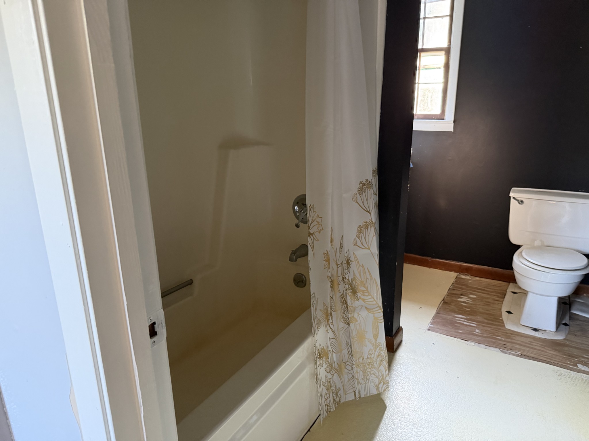 Bathroom with a bathtub behind a floral shower curtain and a toilet beneath a small window.