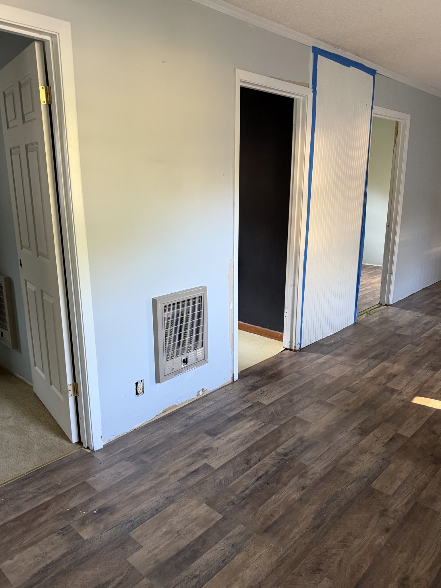 Hallway with wood-look flooring, open doorways, and a beadboard panel taped for painting.