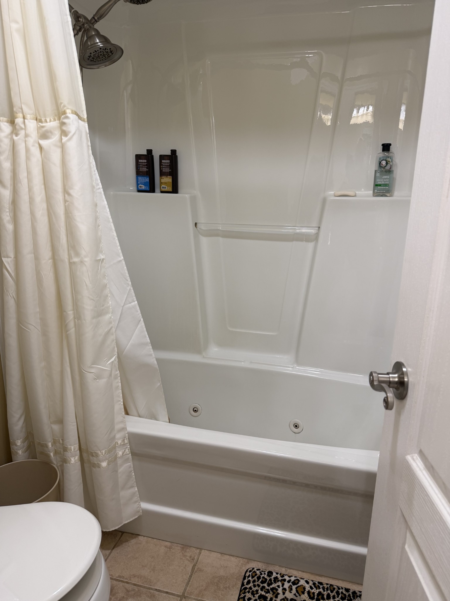 Bathroom with a jetted tub and shower, built-in shelves, and white curtain.