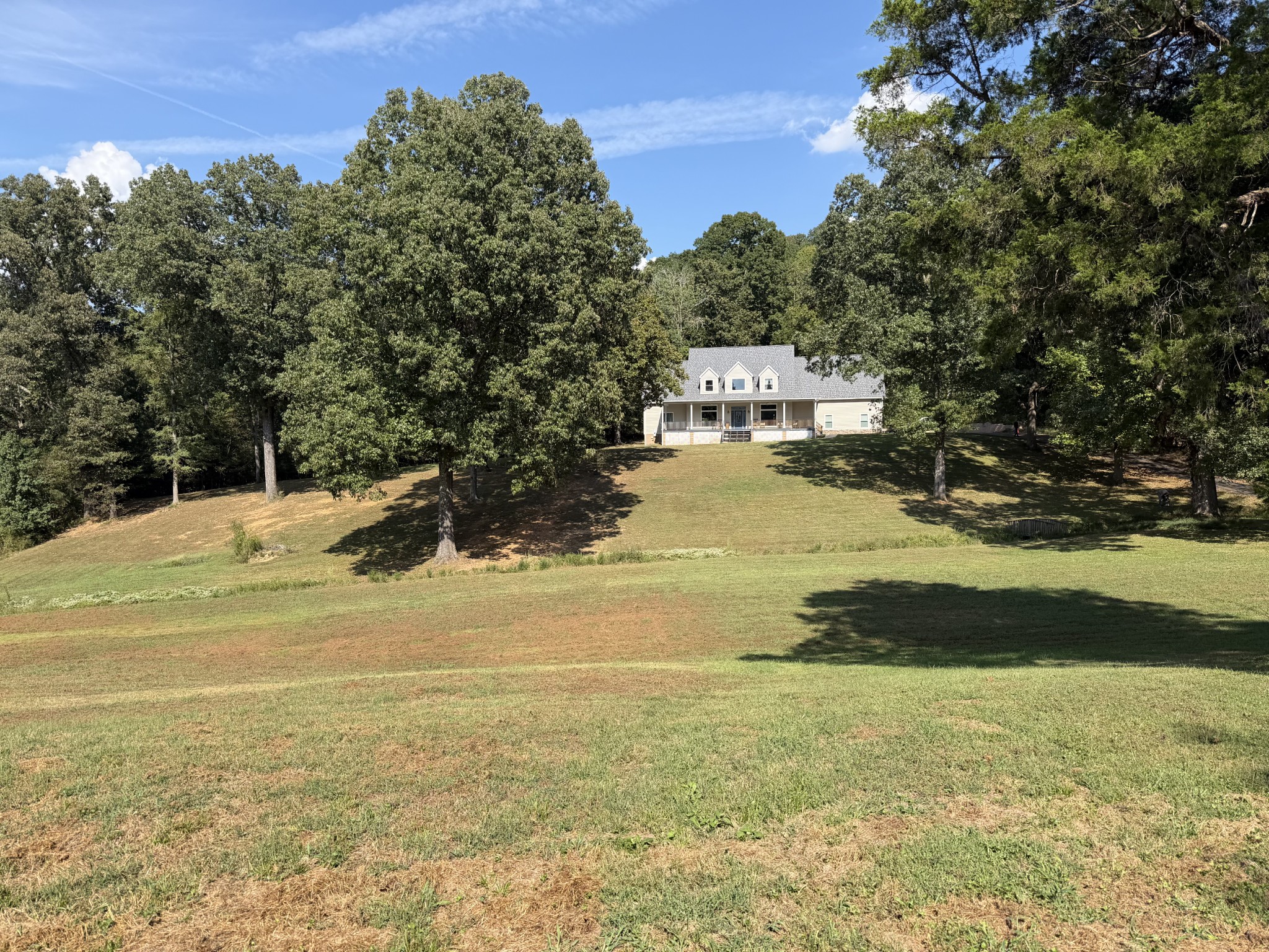 House with a covered front porch set among mature trees above a broad sloping lawn.