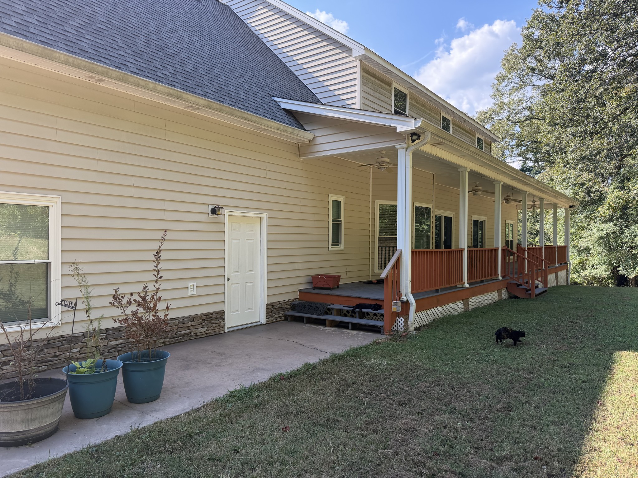 House exterior with a long covered porch and reddish-brown railings beside a grassy yard.