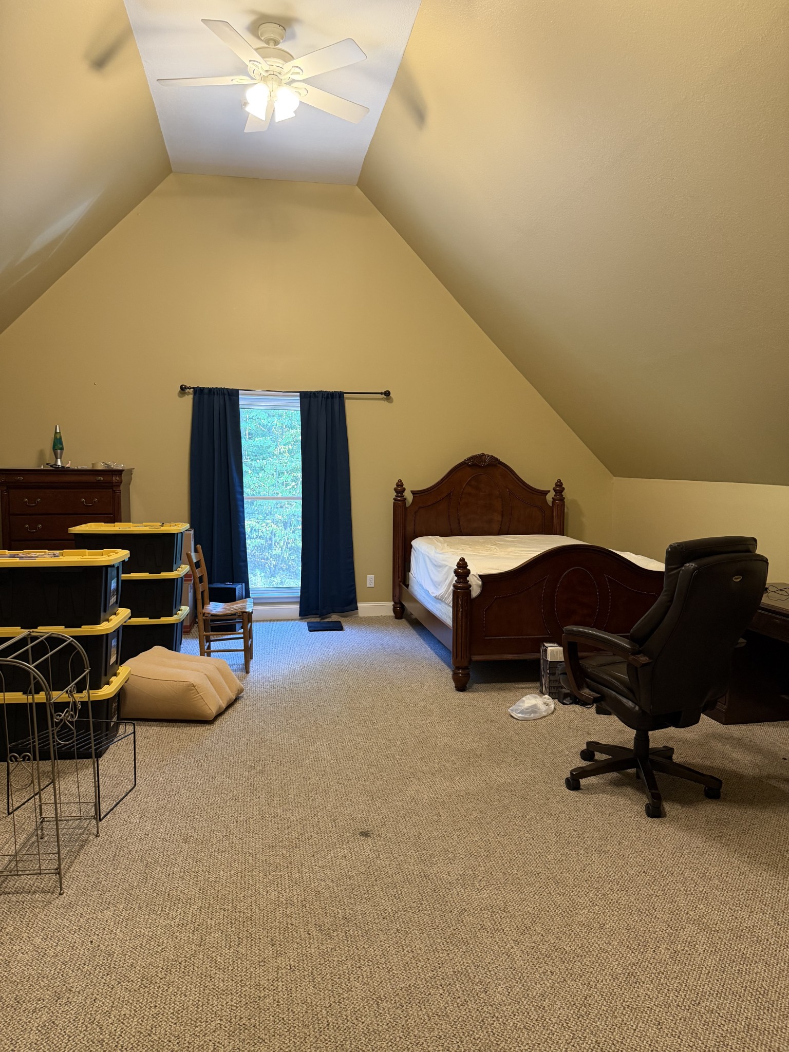 Bedroom with a steep sloped ceiling, dark wooden bed, and tall window with navy curtains.