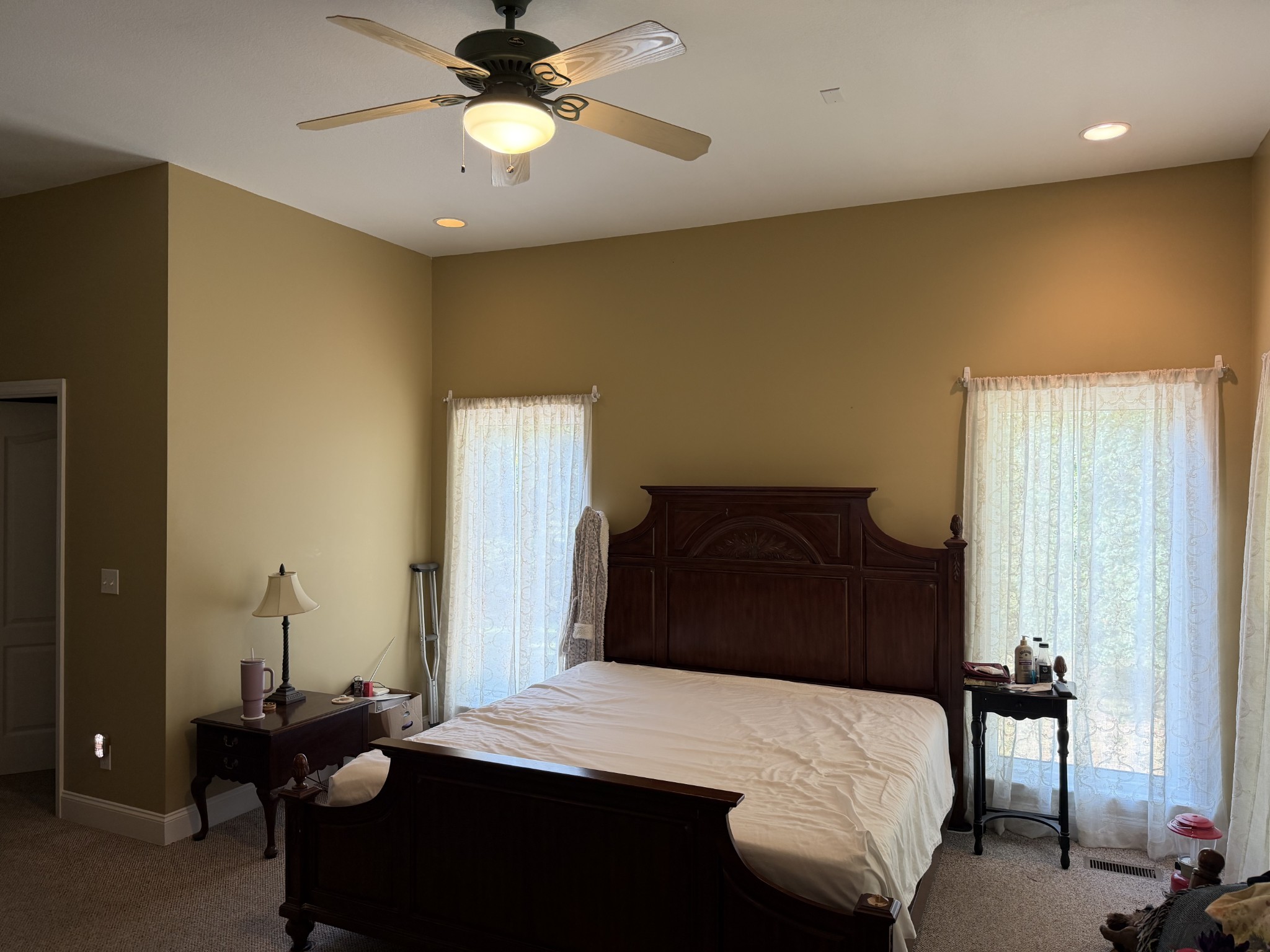 Bedroom with a dark wood bed, carved headboard, lace curtains, and ceiling fan.