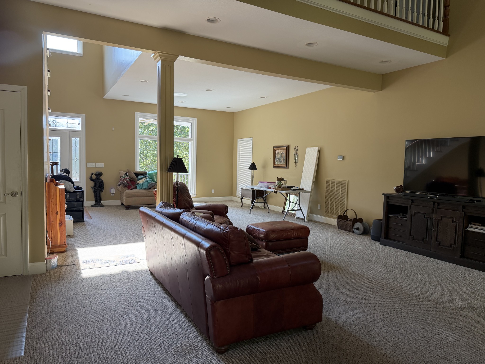 Furnished living room with brown leather seating, a tall column, and an open loft above.