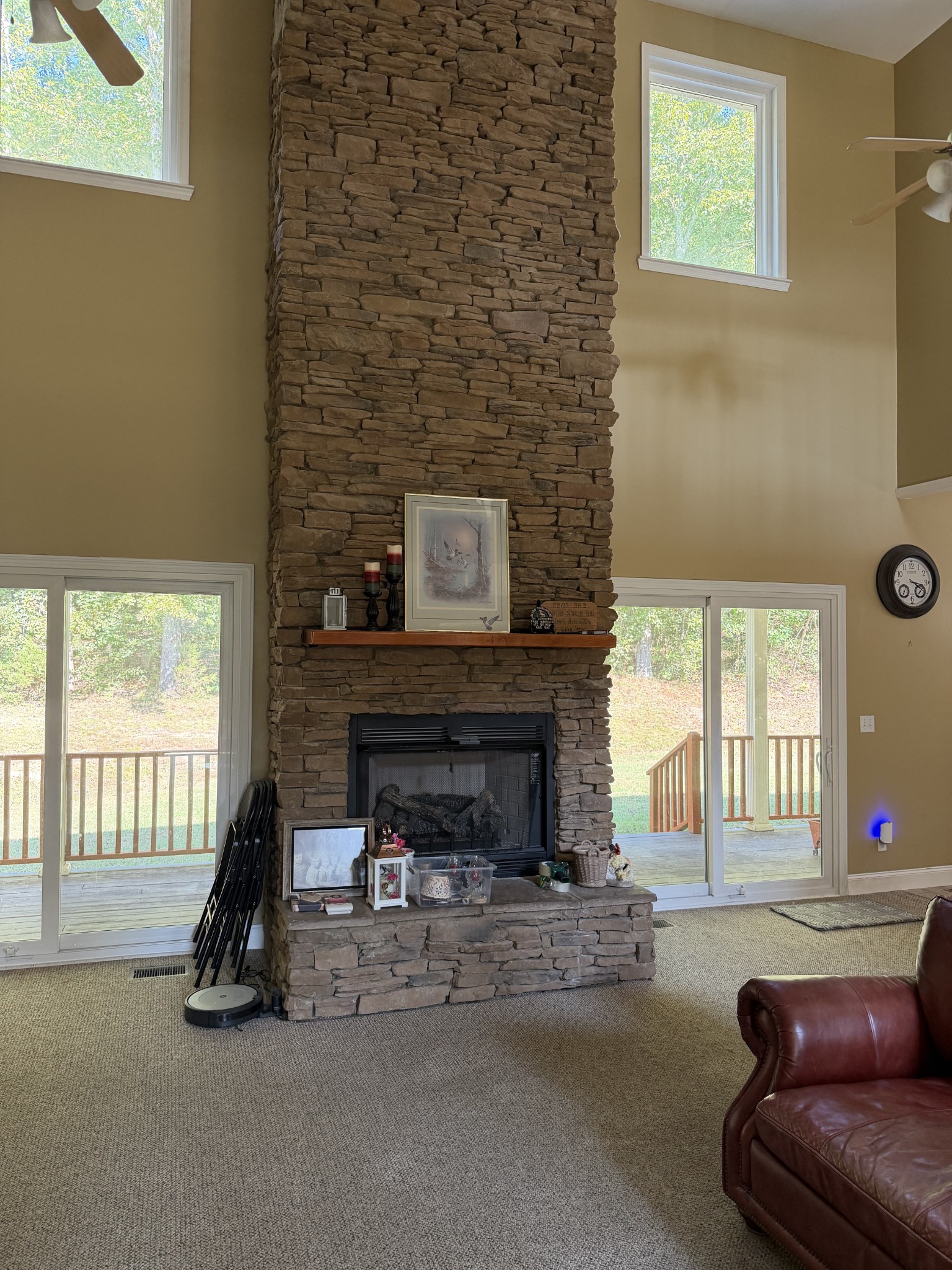 Living room with a tall stone fireplace between large windows and sliding glass doors.