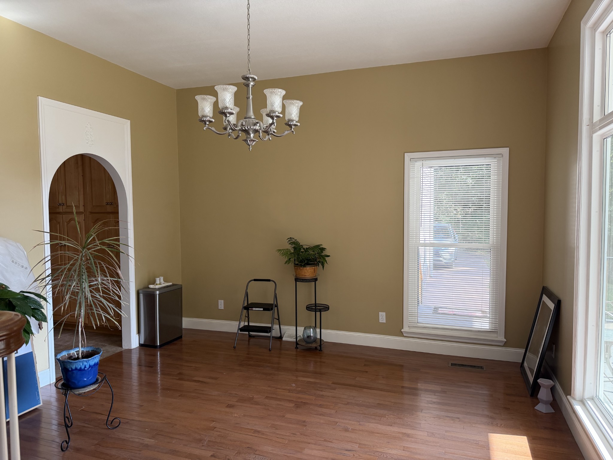 Mostly empty dining room with hardwood floors, chandelier, arched doorway, and tall windows.