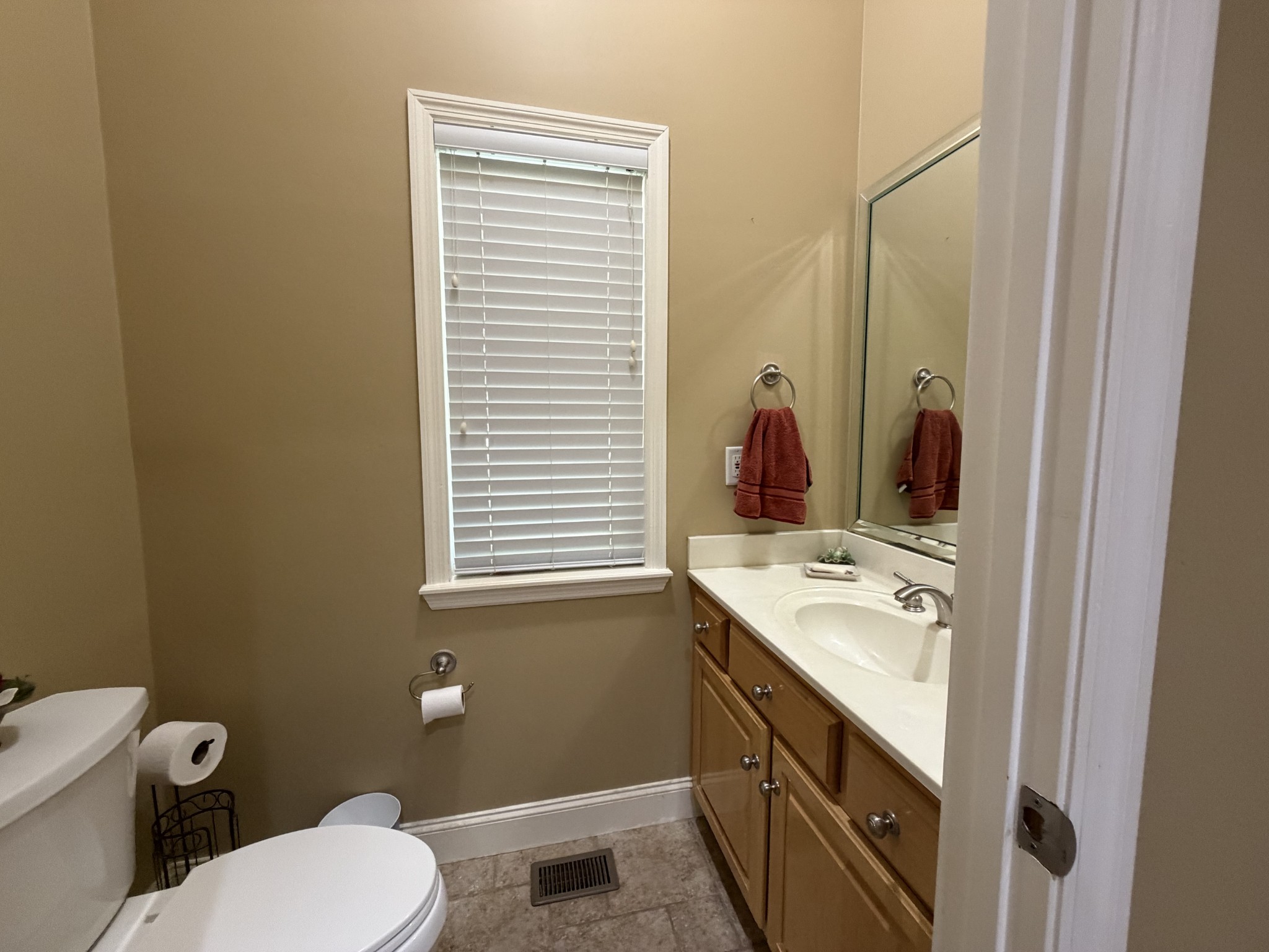 Bathroom with a wood vanity, white sink, mirrored wall, and window with blinds.