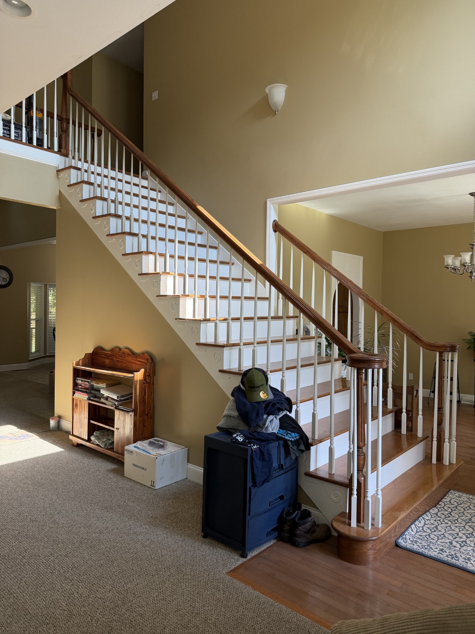 Two-story foyer with a curved wood staircase, white balusters, and clothing piled on a cart.