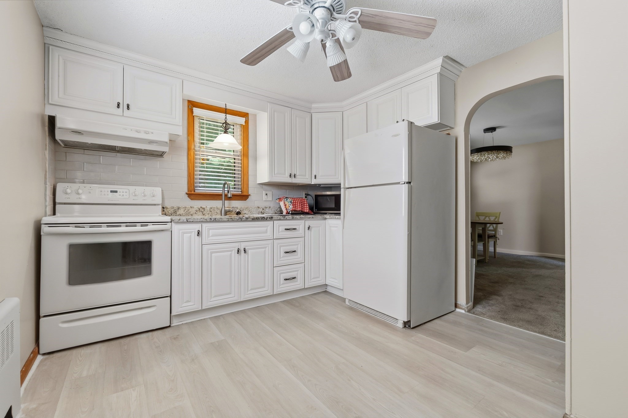 Kitchen with white cabinets, light wood flooring, granite counters, and an arched doorway to the dining area.