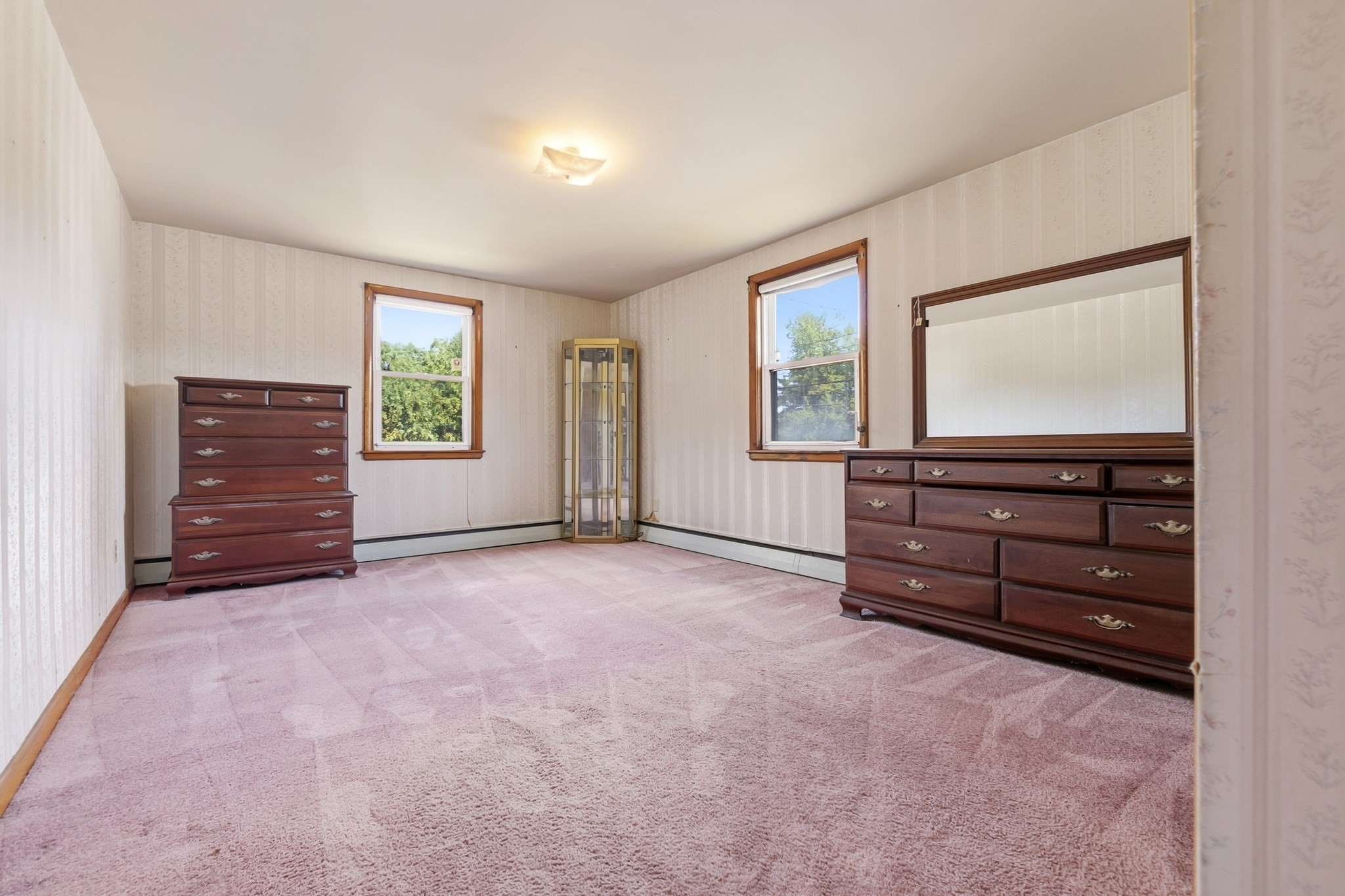 Bedroom with pink carpeting, two windows, and dark wood dressers with a large mirror.